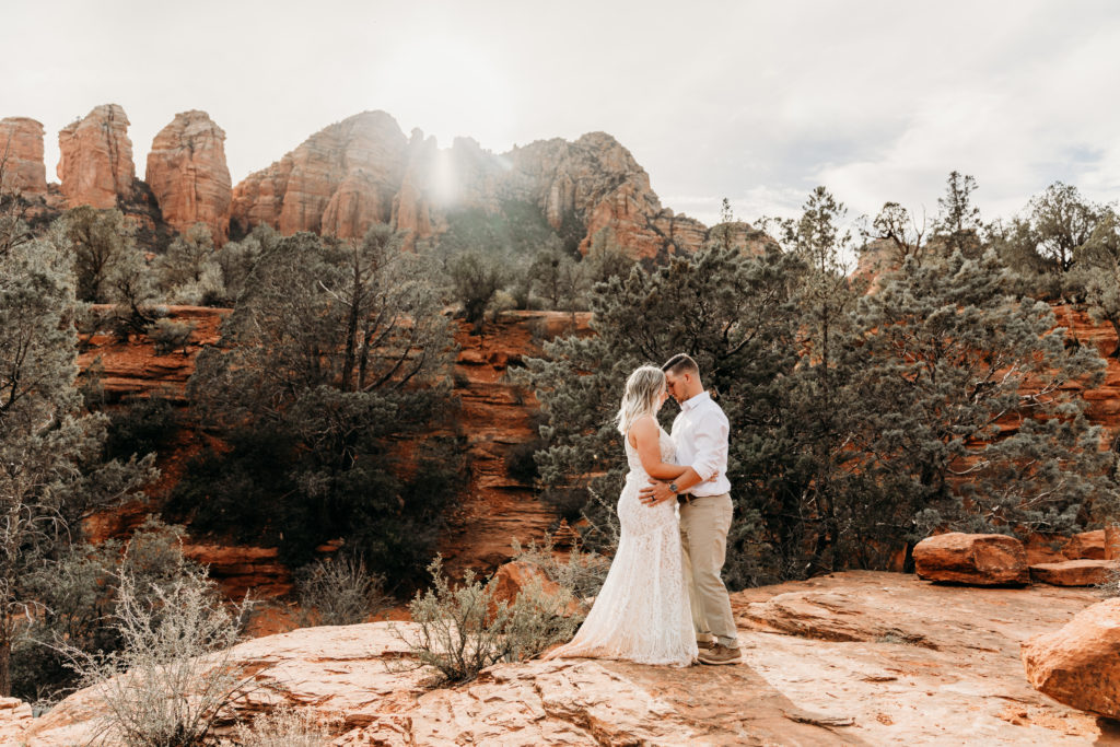 bride and groom embrace with foreheads together in front of tall red rocks at Seven Sacred Pools in Sedona Arizona