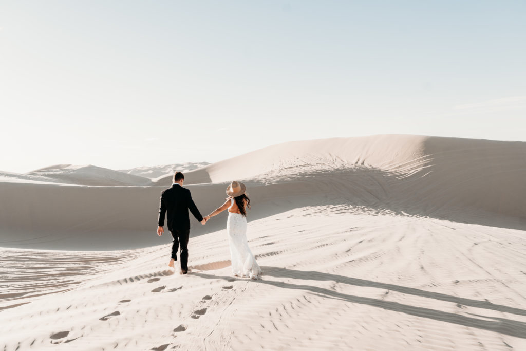 bride holding grooms hand in sand