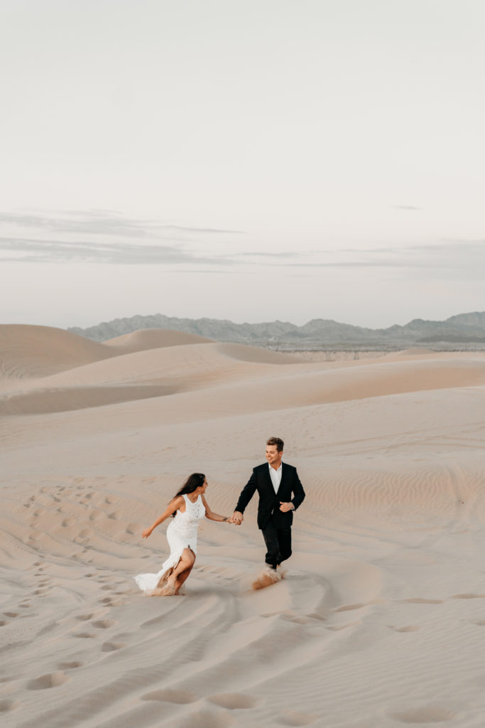 bride and groom running in sand dunes