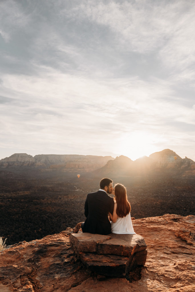 Adventurous elopement in Sedona, Arizona. Couple sitting down watching hot air balloon at sunrise.
