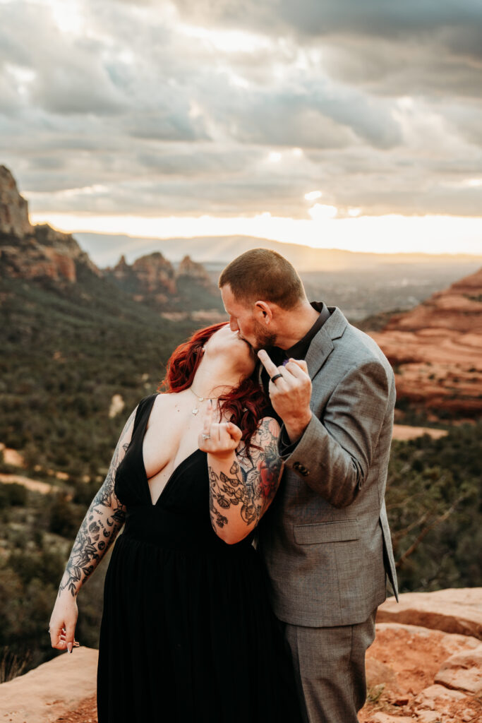 bride and groom showing off their wedding fingers at the camera after eloping at merry go round rock in sedona arizona