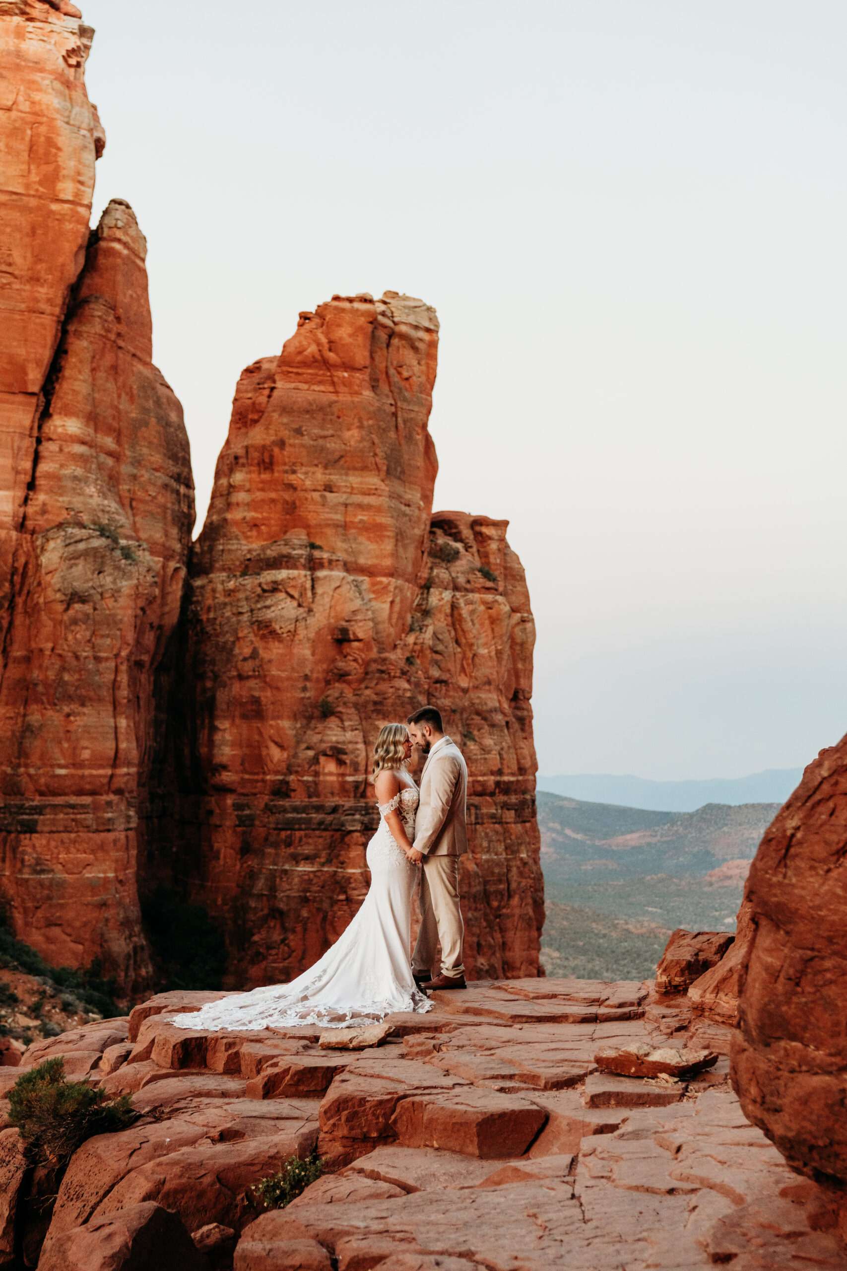 Bride and groom holding hands while standing on a ledge at Cathedral Rock in Sedona arizona after their elopement